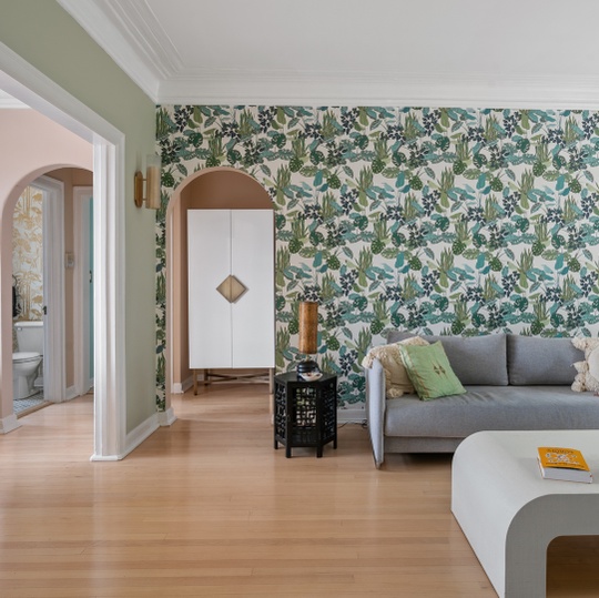 Living room with botanical wallpaper, gray sofa, and arched cabinet alcove.
